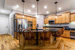 Kitchen featuring light wood-style flooring, a center island with sink, pendant lighting, dark stone counters, and recessed lighting