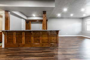 Indoor bar with dark wood finished floors, light stone counters, recessed lighting, and a textured ceiling