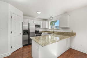 Kitchen with a peninsula, appliances with stainless steel finishes, dark wood-style flooring, light stone counters, and white cabinets