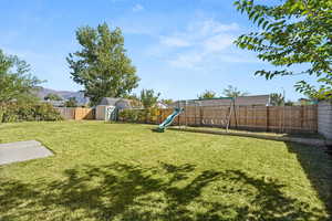 Fenced backyard featuring a storage shed and a playground