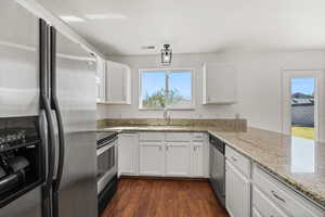 Kitchen with appliances with stainless steel finishes, white cabinets, light stone counters, and dark wood finished floors