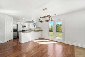 Kitchen with white cabinets, appliances with stainless steel finishes, dark stone countertops, dark wood finished floors, and pendant lighting