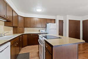 Kitchen with white appliances, a textured ceiling, light wood-type flooring, a kitchen island, and light countertops