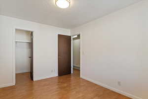 Unfurnished bedroom featuring light wood-type flooring, a textured ceiling, and a walk in closet