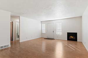 Unfurnished living room featuring a lit fireplace, wood finished floors, and a textured ceiling