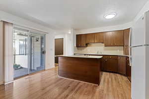 Kitchen with freestanding refrigerator, backsplash, light wood-style floors, a textured ceiling, and a kitchen island