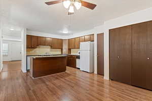 Kitchen featuring white appliances, a kitchen island, backsplash, dark wood-type flooring, and light countertops