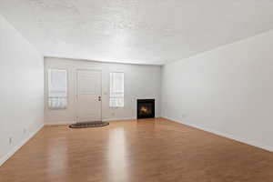 Unfurnished living room featuring a warm lit fireplace, light wood finished floors, and a textured ceiling