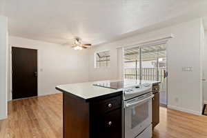 Kitchen with electric stove, dark brown cabinets, light wood-type flooring, a textured ceiling, and a kitchen island
