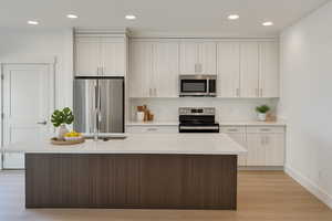 Kitchen with appliances with stainless steel finishes, recessed lighting, light stone counters, light wood-type flooring, and an island with sink