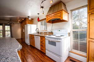 Kitchen featuring white appliances, hanging light fixtures, dark wood-type flooring, custom exhaust hood, and a textured ceiling