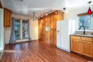 Kitchen with dark wood finished floors, white refrigerator with ice dispenser, brown cabinetry, decorative light fixtures, and a chandelier