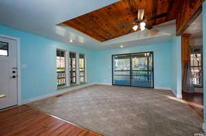 Unfurnished living room featuring wood finished floors, wood ceiling, ceiling fan, a raised ceiling, and vaulted ceiling