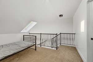 Unfurnished bedroom featuring a skylight, vaulted ceiling, and carpet flooring
