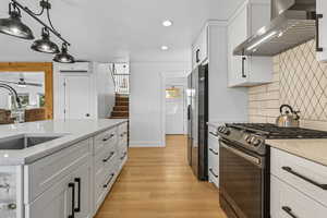 Kitchen with white cabinets, stainless steel appliances, wall chimney exhaust hood, pendant lighting, and light stone counters