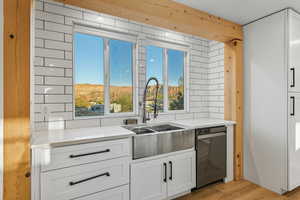 Kitchen featuring white cabinetry, light stone counters, light wood-type flooring, decorative backsplash, and stainless steel dishwasher