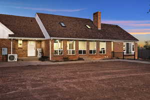 Back of house at dusk with a chimney, brick siding, entry steps, and a patio area
