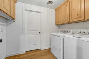 Laundry area featuring light wood finished floors, separate washer and dryer, and cabinet space