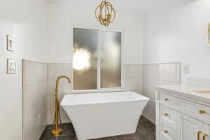 Full bath featuring tile walls, vanity, a freestanding tub, and wainscoting