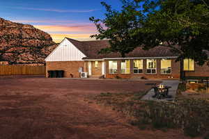 Back of property at dusk featuring a patio area, a fire pit, brick siding, and board and batten siding