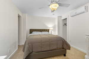 Carpeted bedroom with a wall mounted AC and a ceiling fan