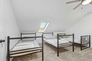 Bedroom with a skylight, light colored carpet, vaulted ceiling, and ceiling fan