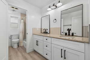 Bathroom with shower / bathtub combination with curtain, double vanity, and light wood-type flooring