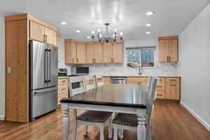 Kitchen with light brown cabinetry, stainless steel appliances, a textured ceiling, pendant lighting, and light stone countertops