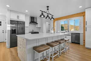 Kitchen with decorative backsplash, fridge with ice dispenser, white cabinets, light wood-style floors, and recessed lighting
