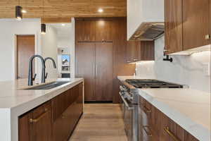 Kitchen with light stone countertops, stainless steel range, pendant lighting, light wood finished floors, and wall chimney range hood