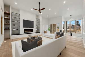 Living area featuring recessed lighting, a warm lit fireplace, built in features, light wood-style floors, and a ceiling fan