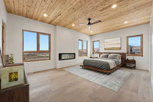 Bedroom featuring wooden ceiling, multiple windows, recessed lighting, a glass covered fireplace, and light wood-style flooring