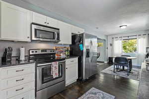 Kitchen featuring appliances with stainless steel finishes, white cabinetry, dark wood-type flooring, dark stone counters, and a textured ceiling