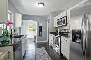 Kitchen with stainless steel appliances, arched walkways, dark stone counters, white cabinets, and dark wood-style floors