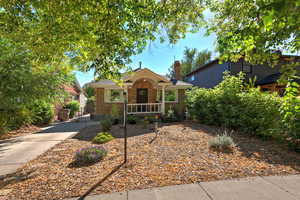 View of front of house with brick siding, covered porch, concrete driveway, and a chimney