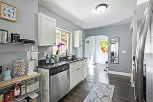 Kitchen featuring arched walkways, stainless steel appliances, white cabinetry, dark wood-style flooring, and dark stone countertops