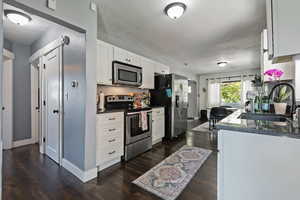 Kitchen featuring white cabinetry, appliances with stainless steel finishes, dark stone counters, and dark wood finished floors
