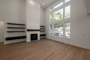 Unfurnished living room featuring a towering ceiling, light wood-style floors, a glass covered fireplace, and recessed lighting