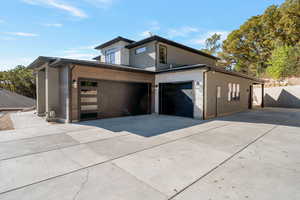 View of side of property featuring driveway, stone siding, a garage, and stucco siding
