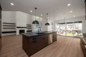 Kitchen with recessed lighting, decorative light fixtures, open floor plan, light wood-type flooring, and a center island with sink