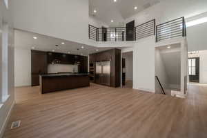 Kitchen with open floor plan, dark countertops, a towering ceiling, recessed lighting, and light wood-style floors