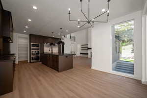 Kitchen with open floor plan, hanging light fixtures, dark countertops, dark brown cabinetry, and a kitchen island with sink