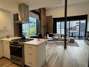 Kitchen with white cabinets, stainless steel gas stove, island range hood, a peninsula, and light wood-type flooring