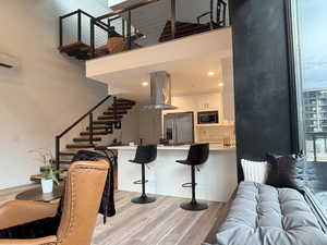 Kitchen featuring island range hood, stainless steel fridge with ice dispenser, light countertops, a breakfast bar, and white cabinets