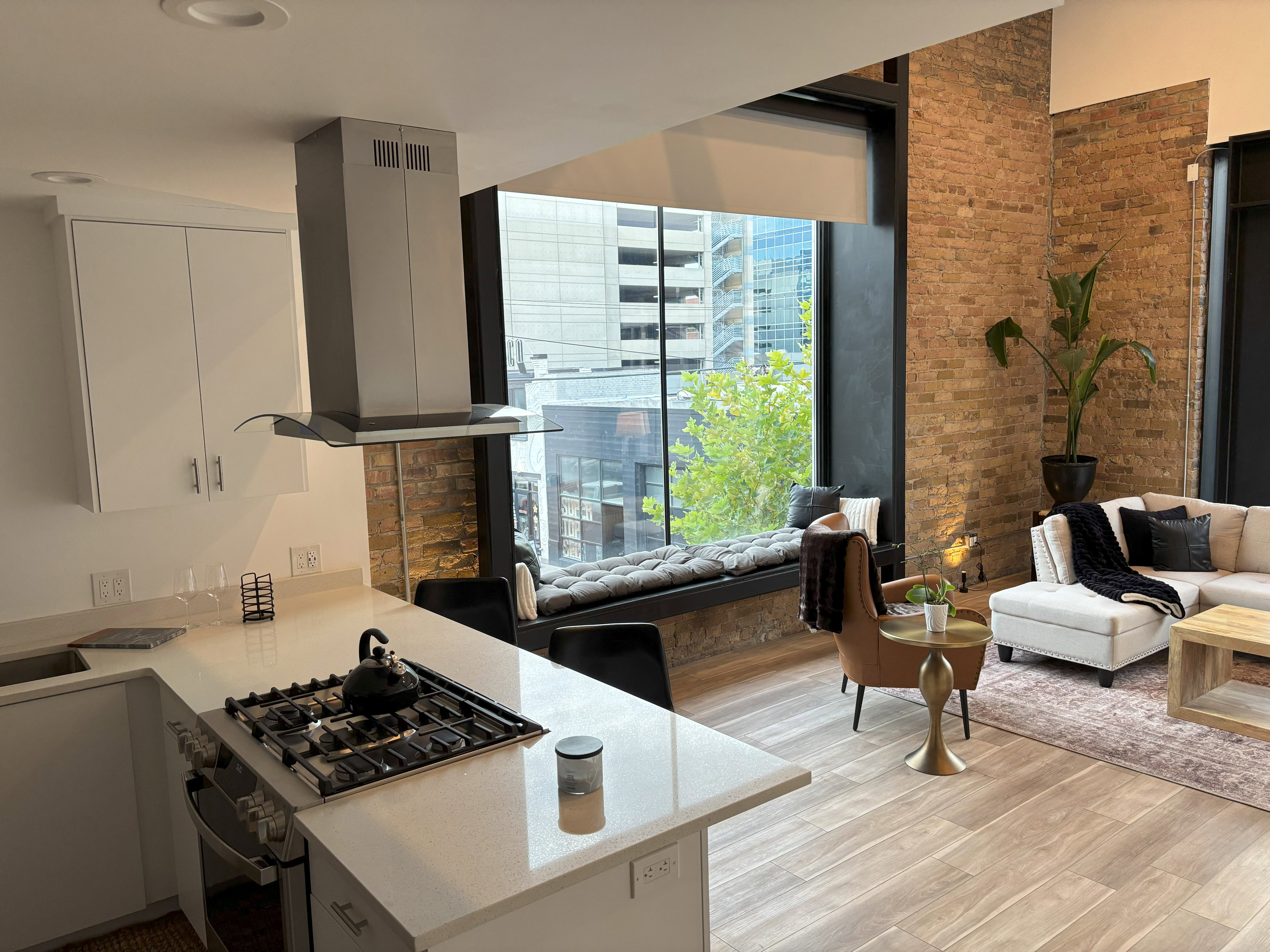 Kitchen with stainless steel range with gas cooktop, wall chimney range hood, light wood-style floors, light stone countertops, and brick wall