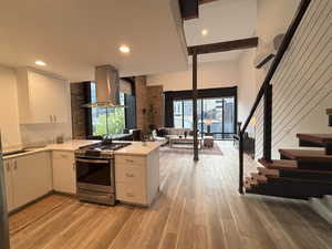 Kitchen with white cabinets, stainless steel gas range oven, ventilation hood, light wood-style floors, and a peninsula