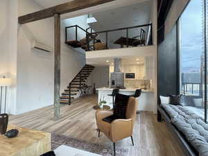 Living area featuring light wood finished floors, a towering ceiling, stairs, a wall mounted air conditioner, and beam ceilings