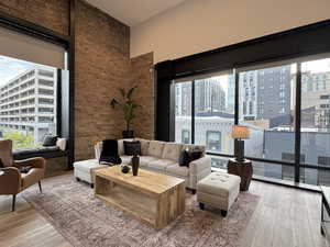 Living area with light wood-type flooring, towering windows, city views, a towering ceiling, and brick wall