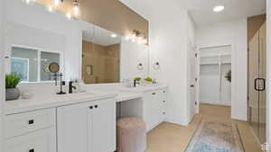 Full bathroom with two vanities, a spacious closet, recessed lighting, and a stall shower