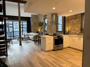 Kitchen featuring plenty of natural light, wall chimney exhaust hood, gas range, white cabinets, and recessed lighting